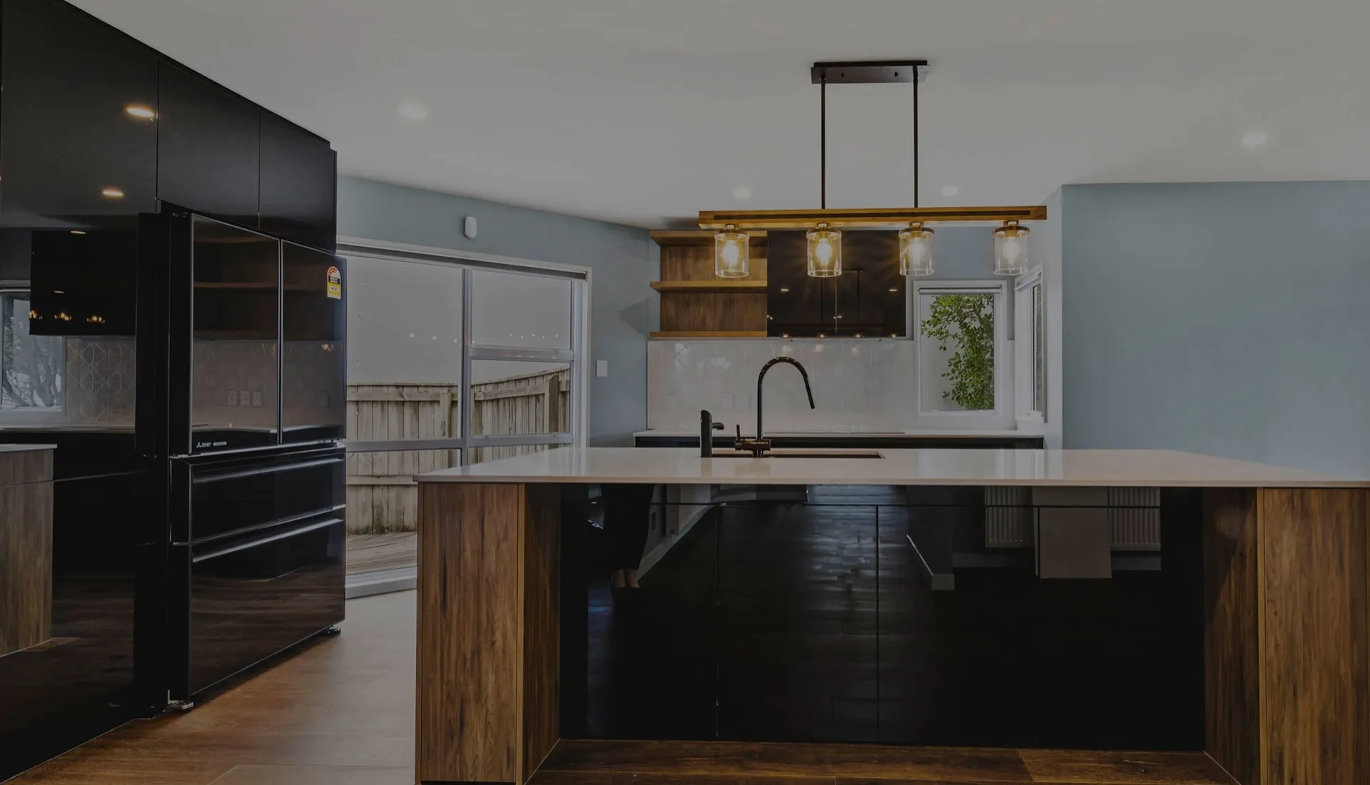 Open-plan kitchen with gloss black cabinetry, a timber-clad island with a pale stone worktop and a row of glass pendant lights