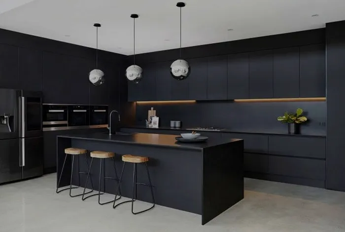 Matt black handleless kitchen with a waterfall island, three timber bar stools and warm under-cabinet lighting